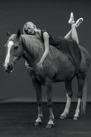 A black and white photograph capturing graceful poses with a horse in studio lighting.