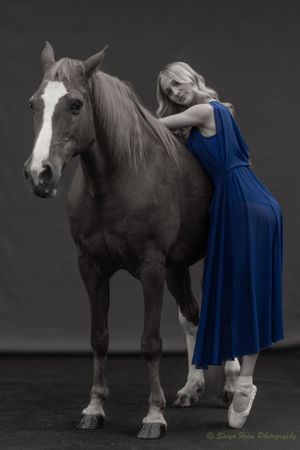 A selective color photograph highlighting a blue dress against a monochrome horse portrait.
