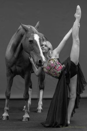 A dancer in an ornate bodice performs a dramatic leg extension beside a majestic horse.