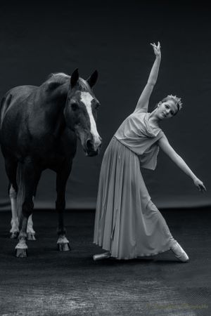 A monochrome portrait of a dancer in flowing dress performing alongside a majestic horse.