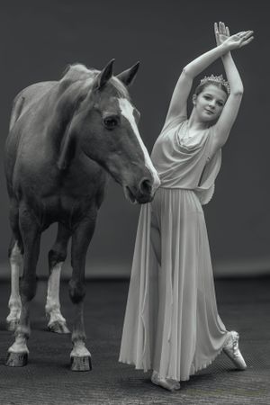 A classical dancer in grey strikes an elegant pose beside a horse in black and white photography.