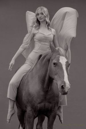 Artistic black and white portrait of dancer in flowing outfit posing on horseback.