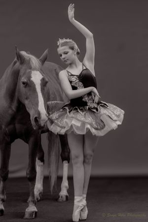 A sepia-toned portrait of a classical ballet dancer posing gracefully beside a horse.