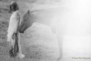 Ethereal misty black and white portrait of person in flowing dress standing beside a horse in a field. Sonya Helm Equine Photography