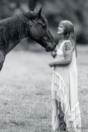 Artistic black and white portrait showing tender moment between horse and person in flowing white dress. Sonya Helm Equine Photography