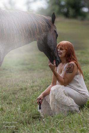 Person in white flowing dress kneeling in grass while interacting with a horse. Sonya Helm Equine Photography, Bristol, TN