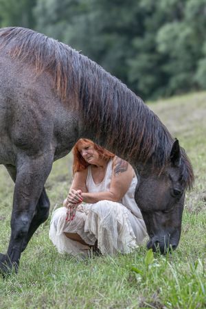 Person in white dress sits peacefully beside grazing horse in sunlit meadow. Sonya Helm Equine Photography, Bristol, TN