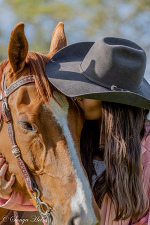 Close-up of horse wearing western bridle with grey cowboy hat and long dark hair visible.