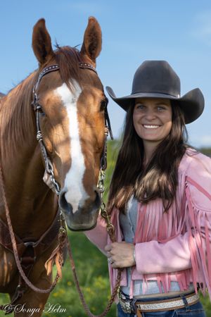 Horse and rider in pink fringe jacket and cowboy hat posing together outdoors.