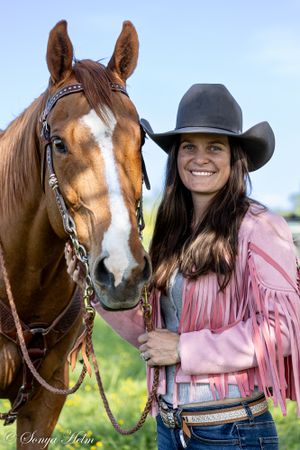 Portrait of chestnut horse with white blaze and rider in pink fringe jacket and cowboy hat.
