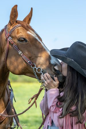 Close-up of tender moment between horse and rider in western gear.