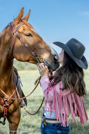 Side view of horse and rider in western attire against blue sky backdrop.