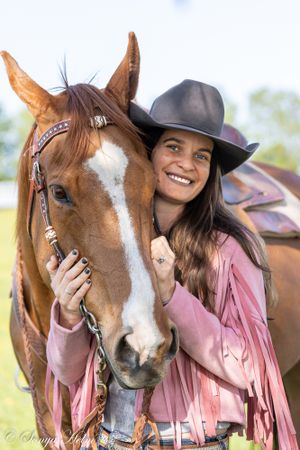Joyful western portrait of horse and rider in pink fringe jacket against bright background.