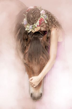 Brown horse wearing dainty pink and white floral decorations against a soft pastel background in dreamy photography style.