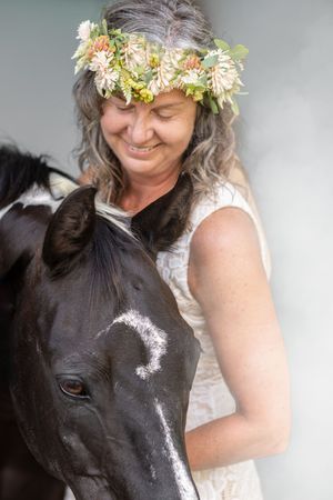 Close up portrait of a black horse and someone wearing white lace and a floral crown.