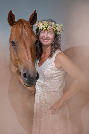 A brown horse and someone wearing a lace dress and floral crown pose together in a series of romantic photos.