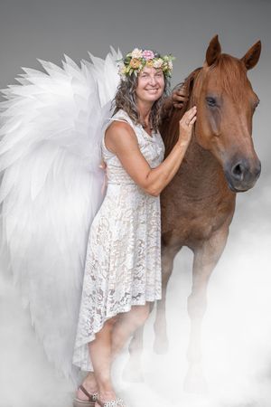 A brown horse and someone in a white lace dress pose together in an ethereal studio photoshoot.