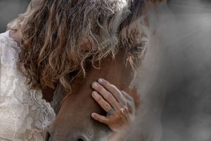 Close-up sideview photo of someone with curly brown hair against a black and gray background.