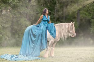 A figure in a flowing blue dress rides a majestic white horse through a misty outdoor setting.