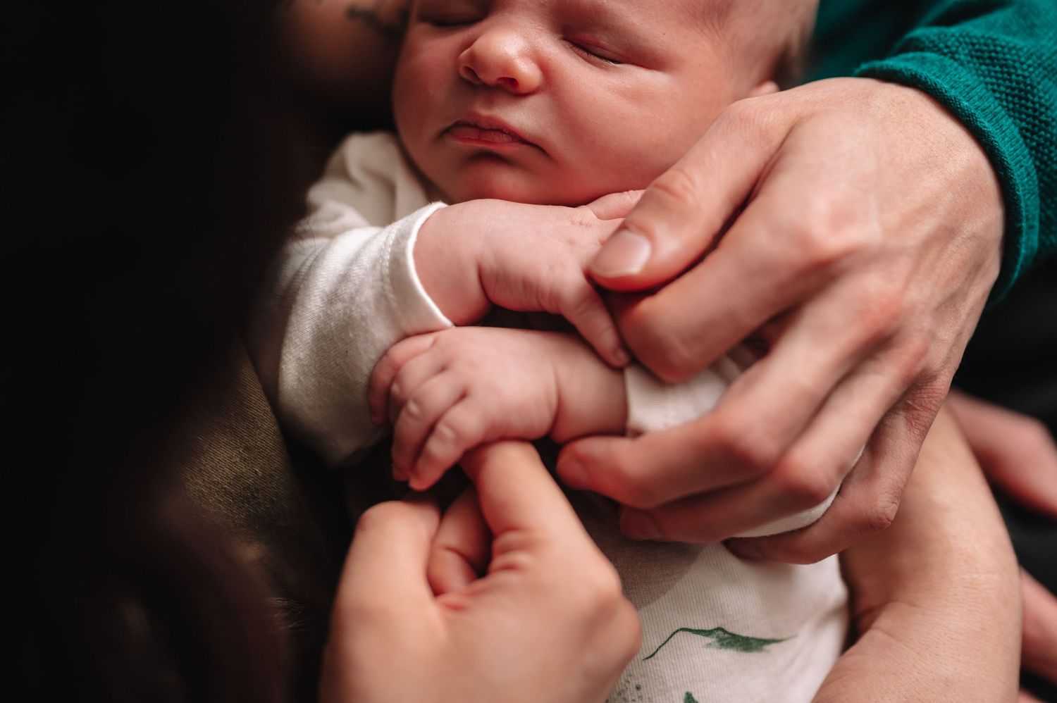 Close up of gentle hands holding newborn baby's tiny fingers.