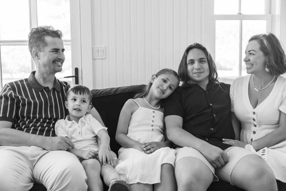Casual family portrait of people relaxing together on a white couch indoors.