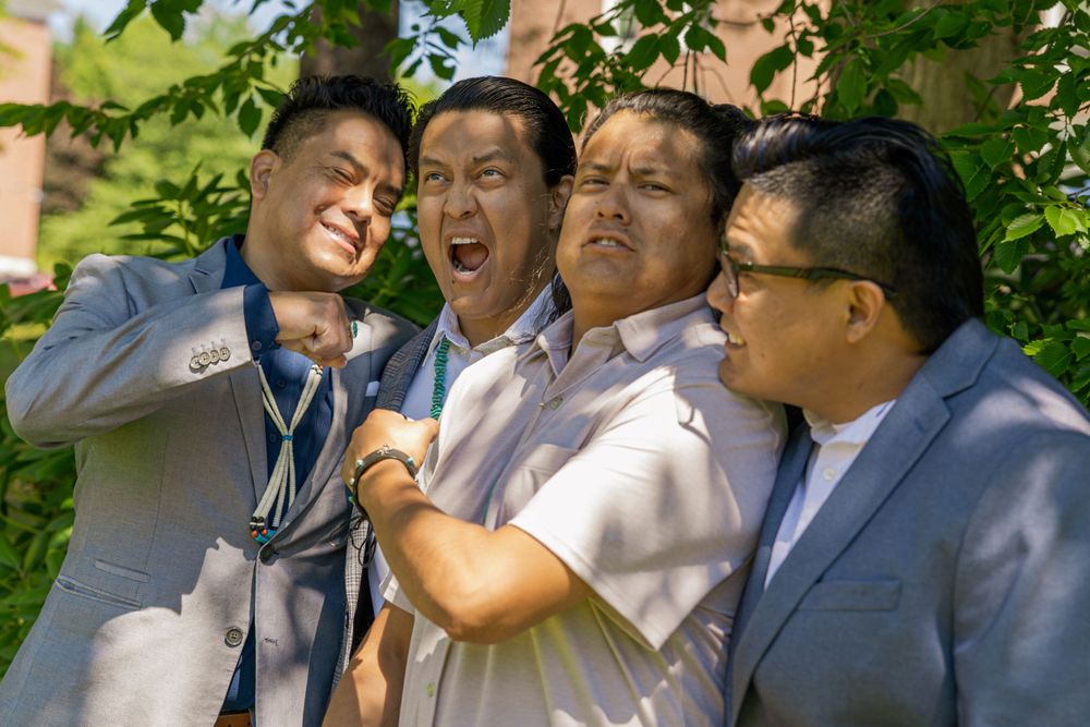 A group of people in formal attire share laughs and candid moments in an outdoor garden setting.