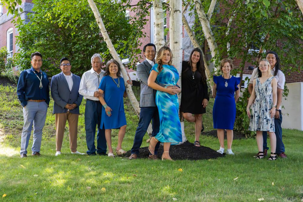 Group of people gathered outdoors on a sunny day near trees and buildings.