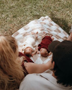 A family resting together on a checkered blanket while watching their sleeping babies.