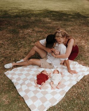 A couple sharing an intimate moment on a picnic blanket while their babies rest nearby.