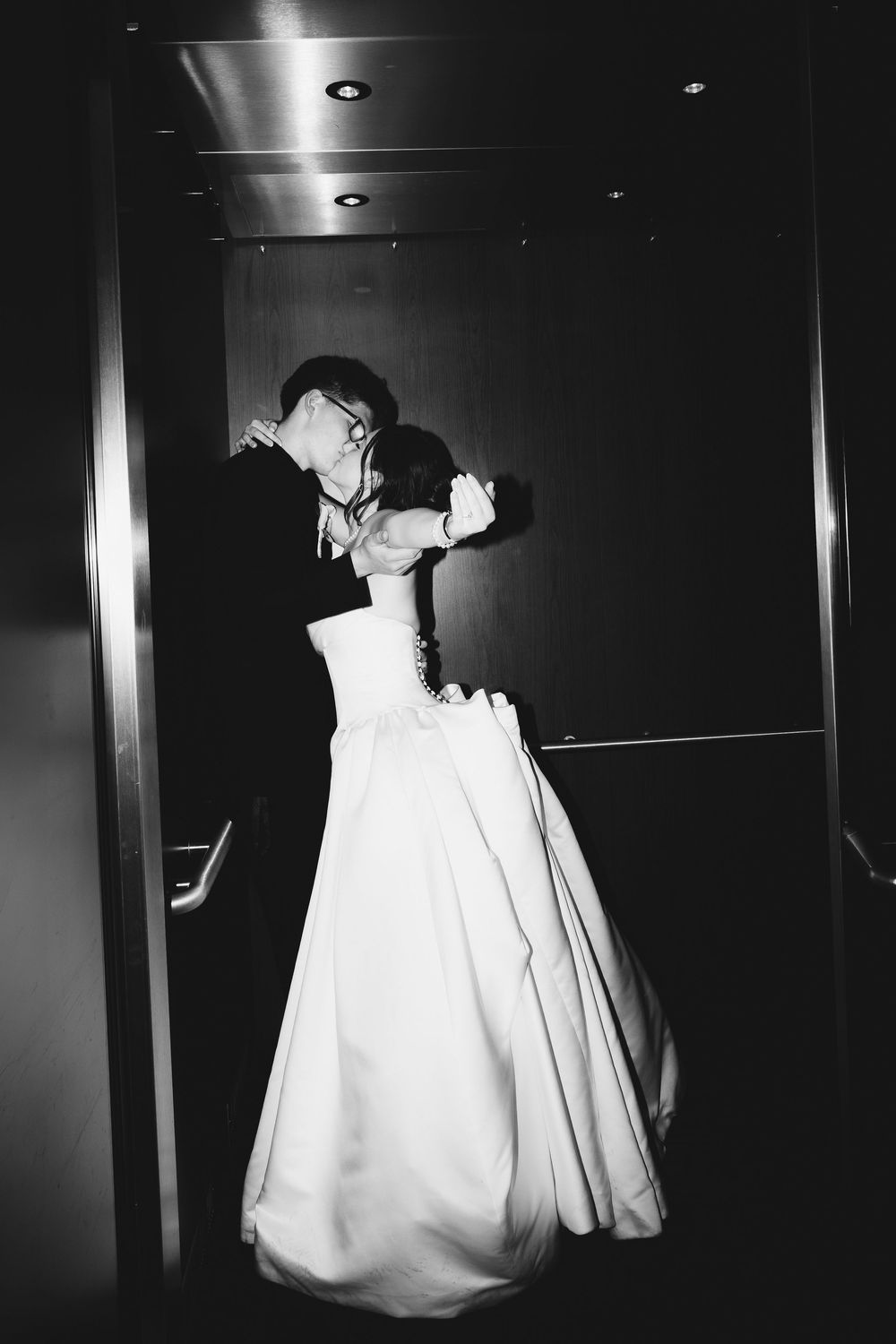 Black and white photo of a bride and groom sharing a romantic kiss in an elevator on their wedding day.