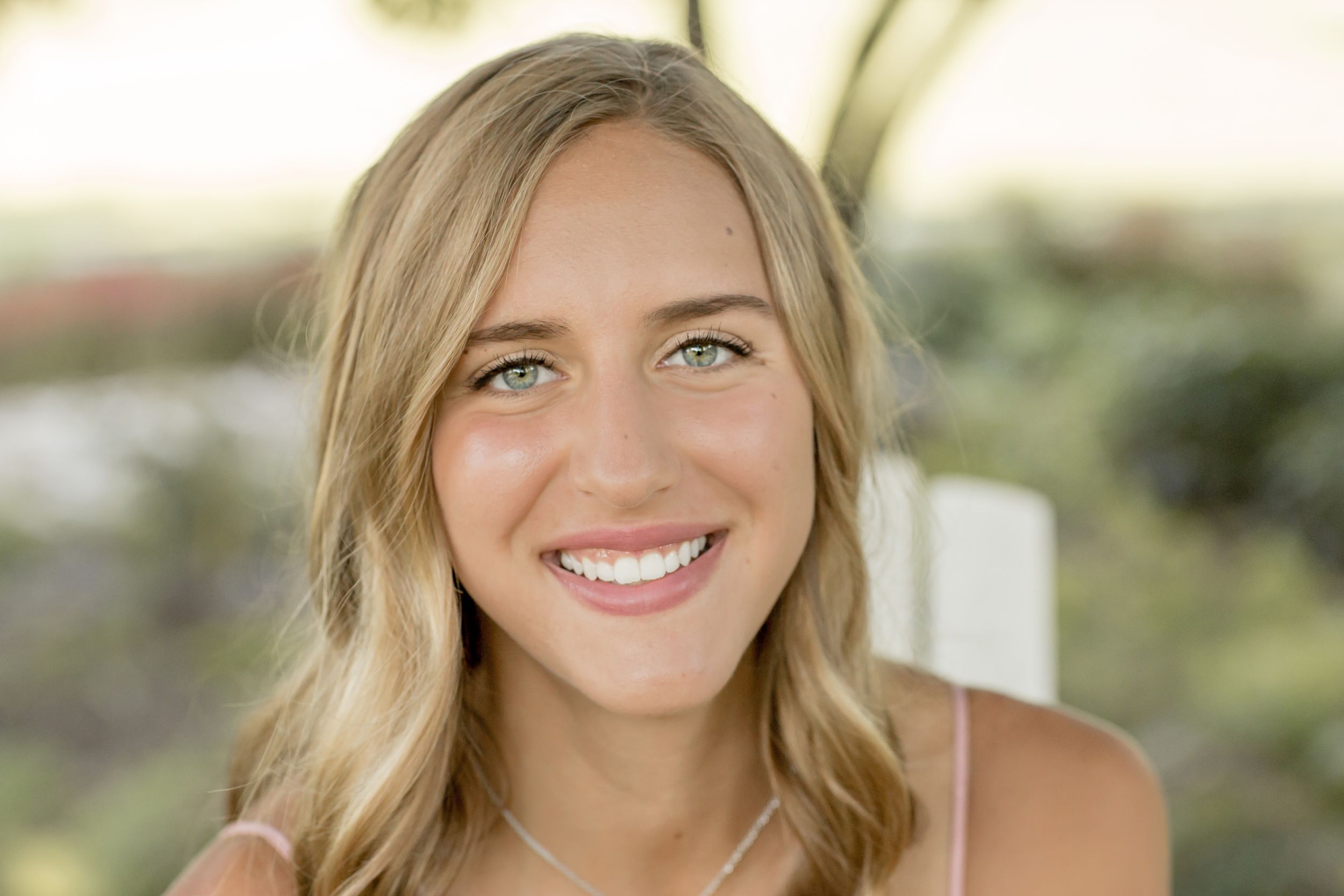Smiling young woman with wavy blonde hair and green eyes in outdoor portrait.