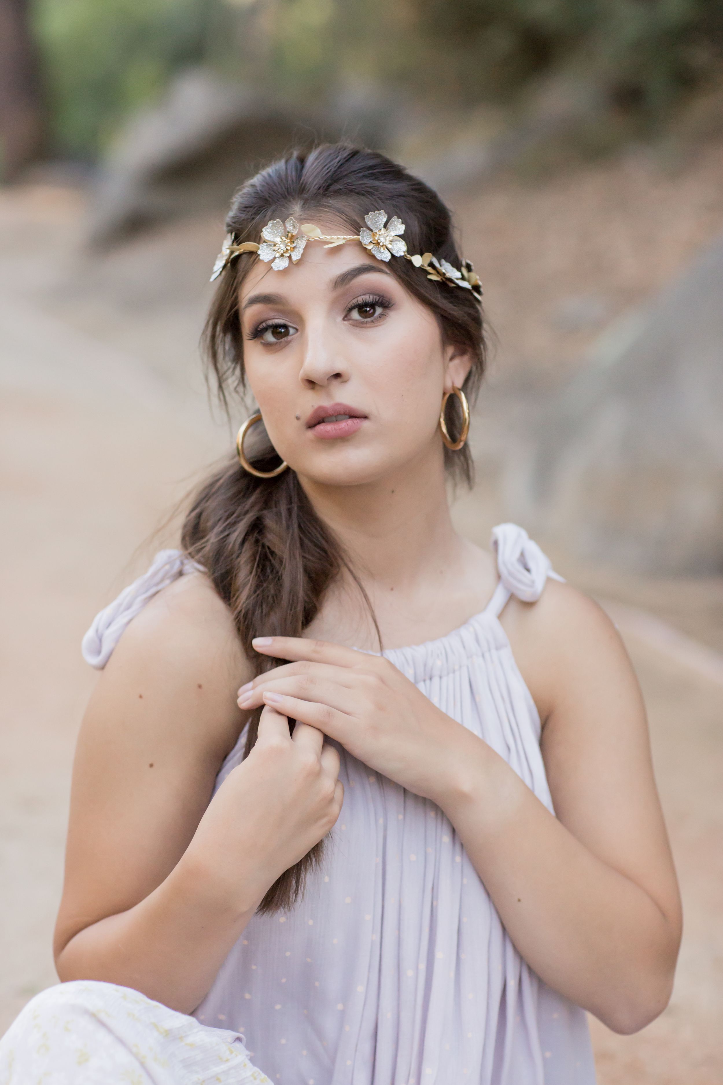 Brunette woman in lavender dress wearing gold floral crown poses outdoors.