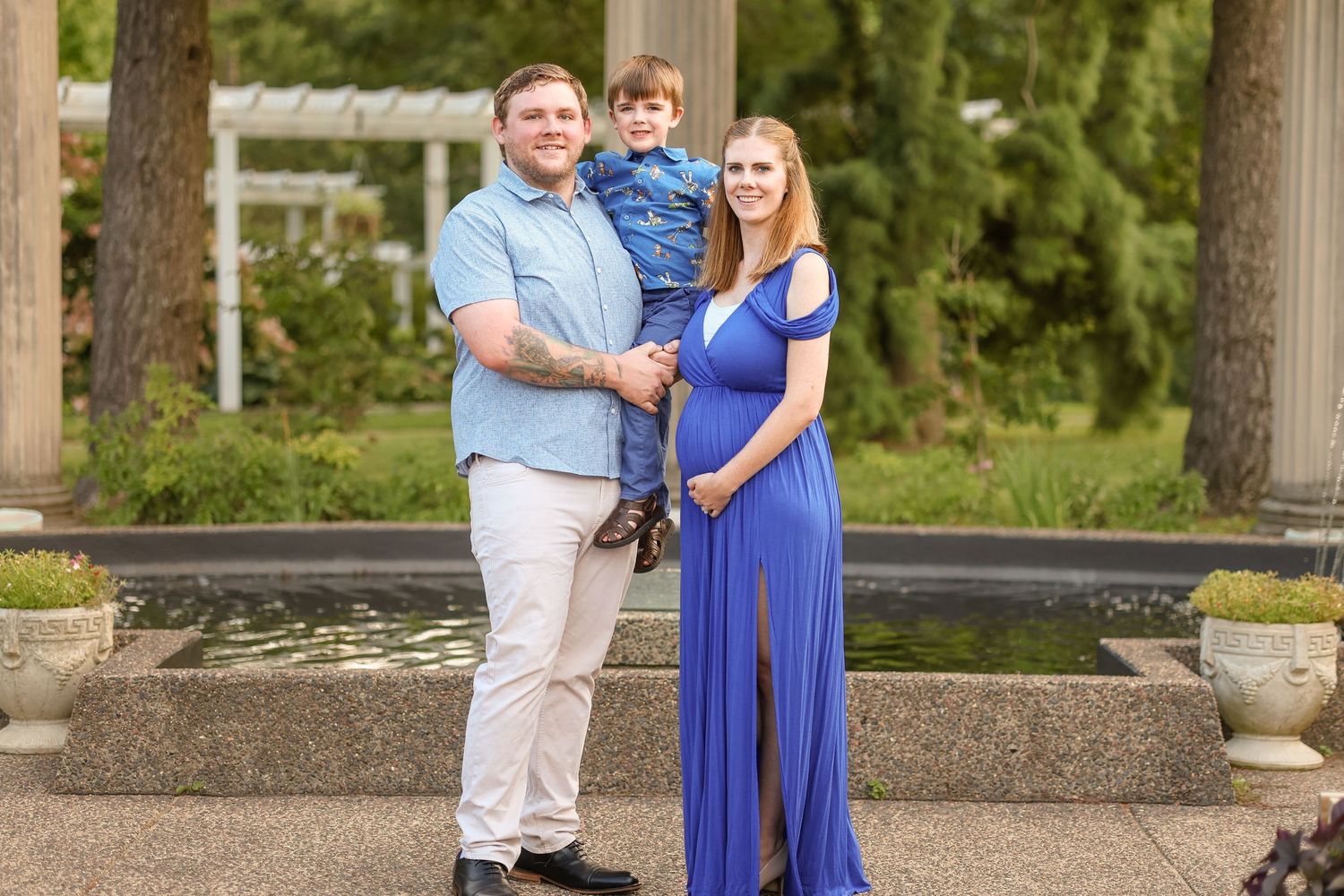 A formal family portrait taken outdoors near a reflecting pool with stone features and trees in the background.