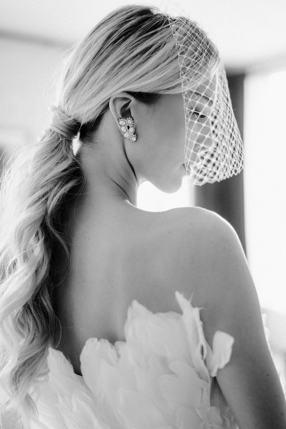 Back view of bride with long blonde hair wearing a veil and strapless wedding dress.