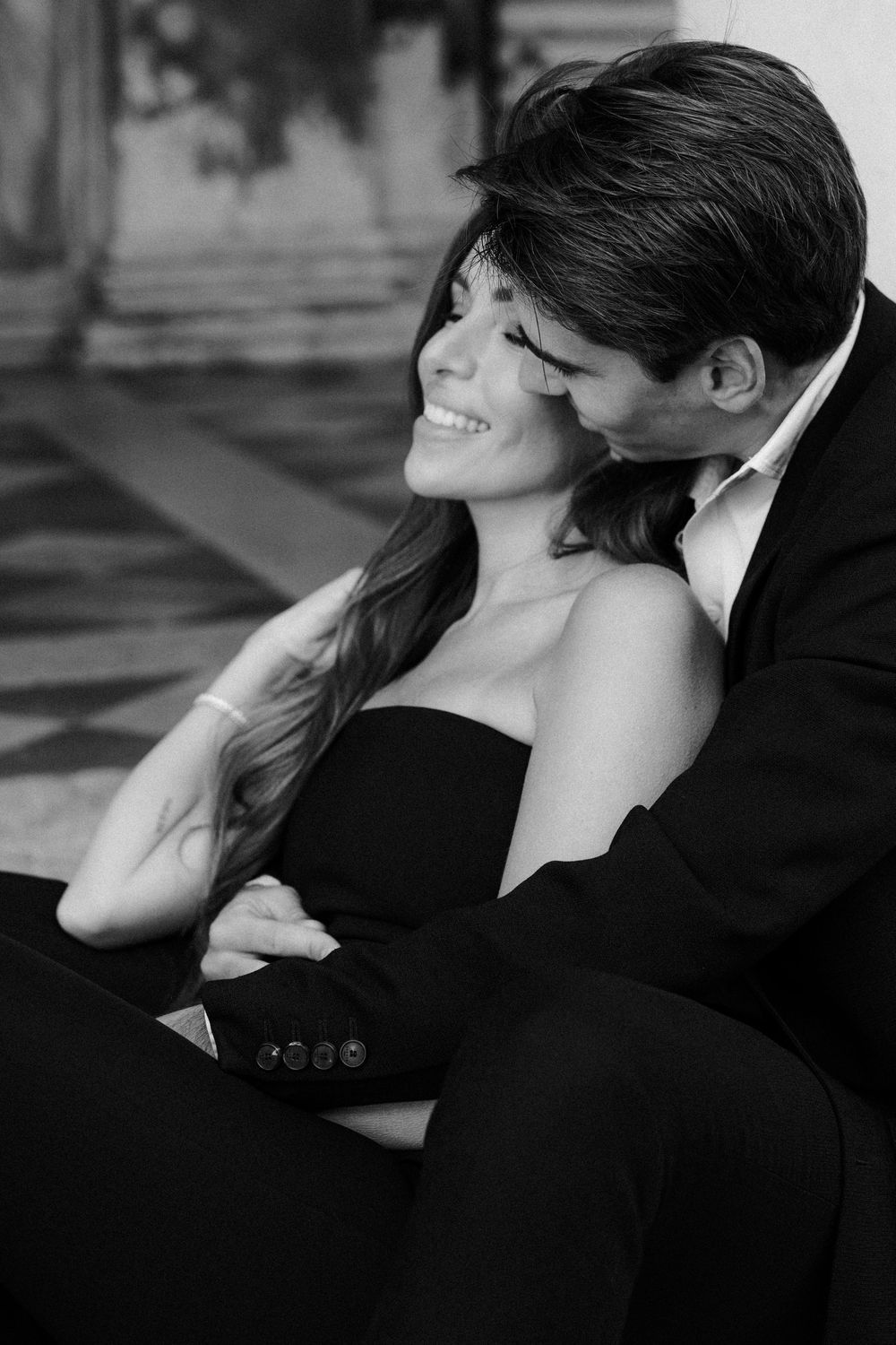 A romantic black and white portrait of a couple embracing, with the woman in a strapless dress smiling joyfully.