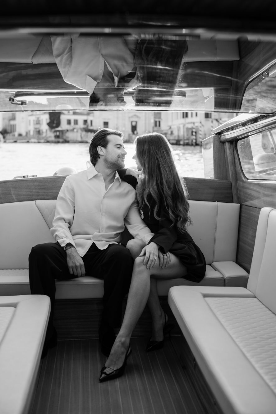 Black and white photo of a romantic couple sitting together on a luxury boat, gazing at each other lovingly.