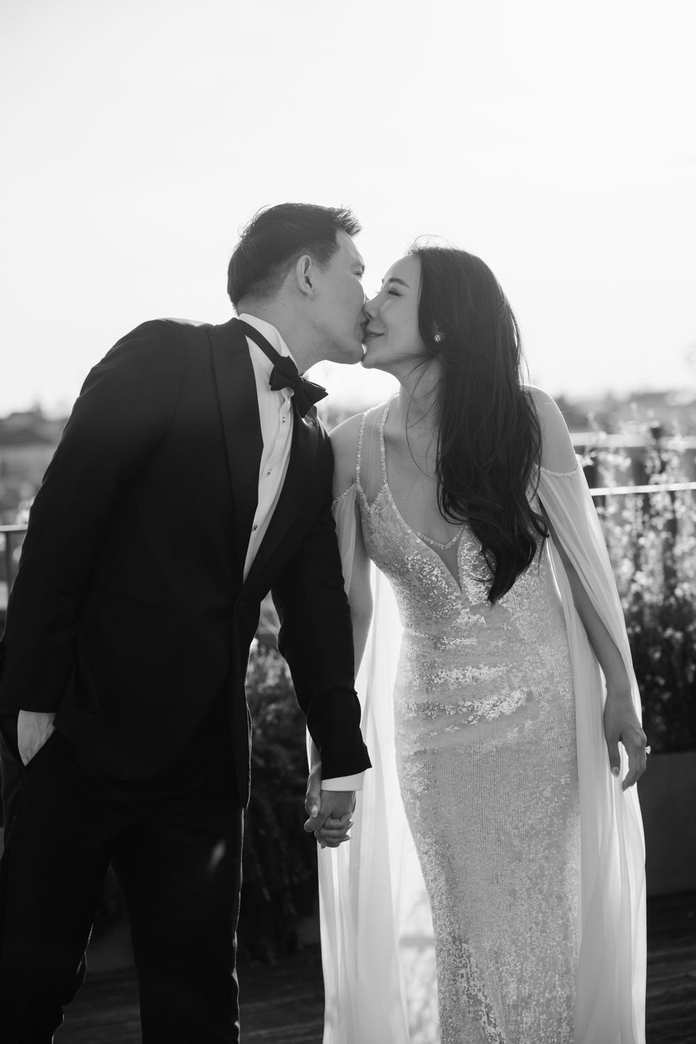 Black and white photo of a couple kissing at their wedding, bride in sequined gown, groom in tuxedo.