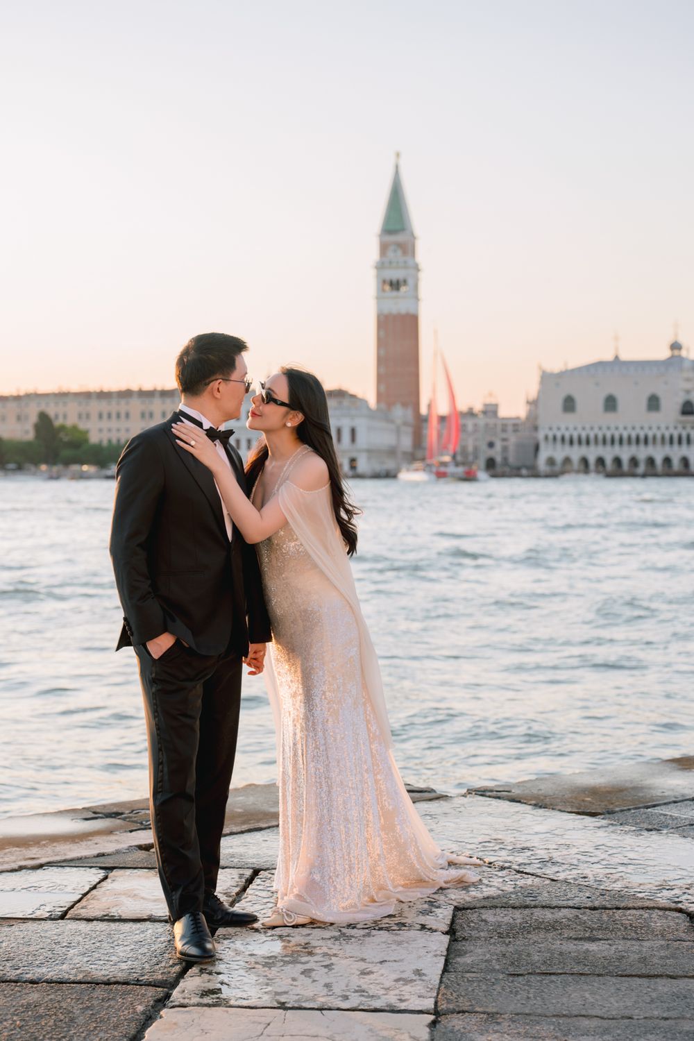 Couple kissing in formal wear on Venice waterfront with St. Mark's Campanile at sunset.