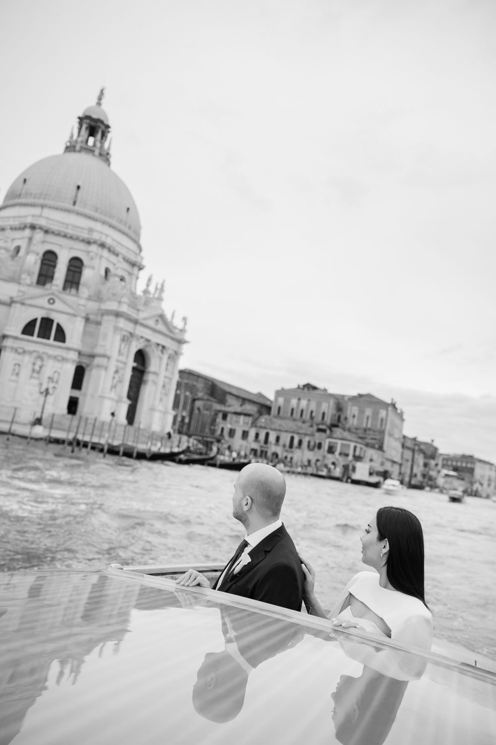Black and white photo of a couple on a boat in Venice with the Santa Maria della Salute basilica in the background.