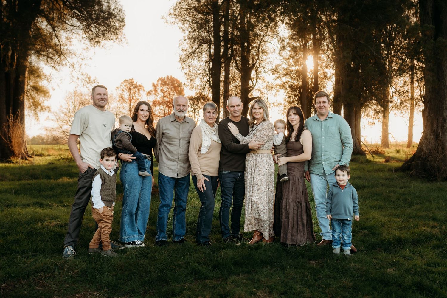 Extended family gathering outdoors at sunset with glowing autumn trees in background.