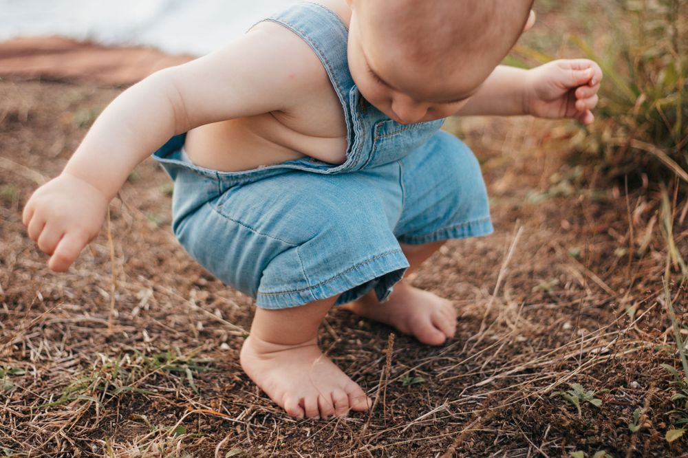Close up of small bare feet and blue overalls against dirt ground.