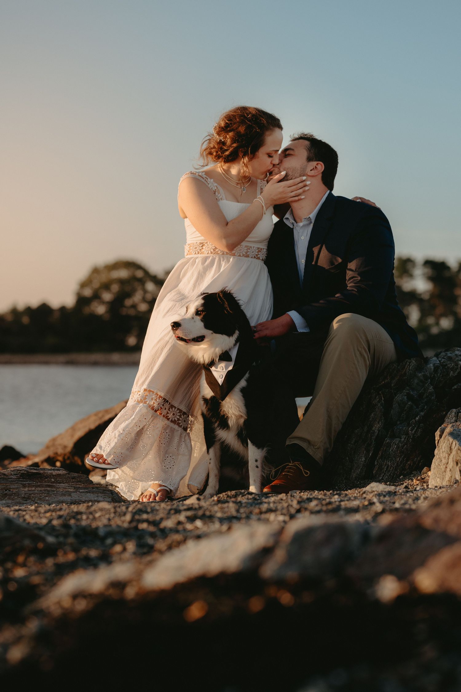 Bride and groom kiss between towering stone columns in dramatic light at formal venue.