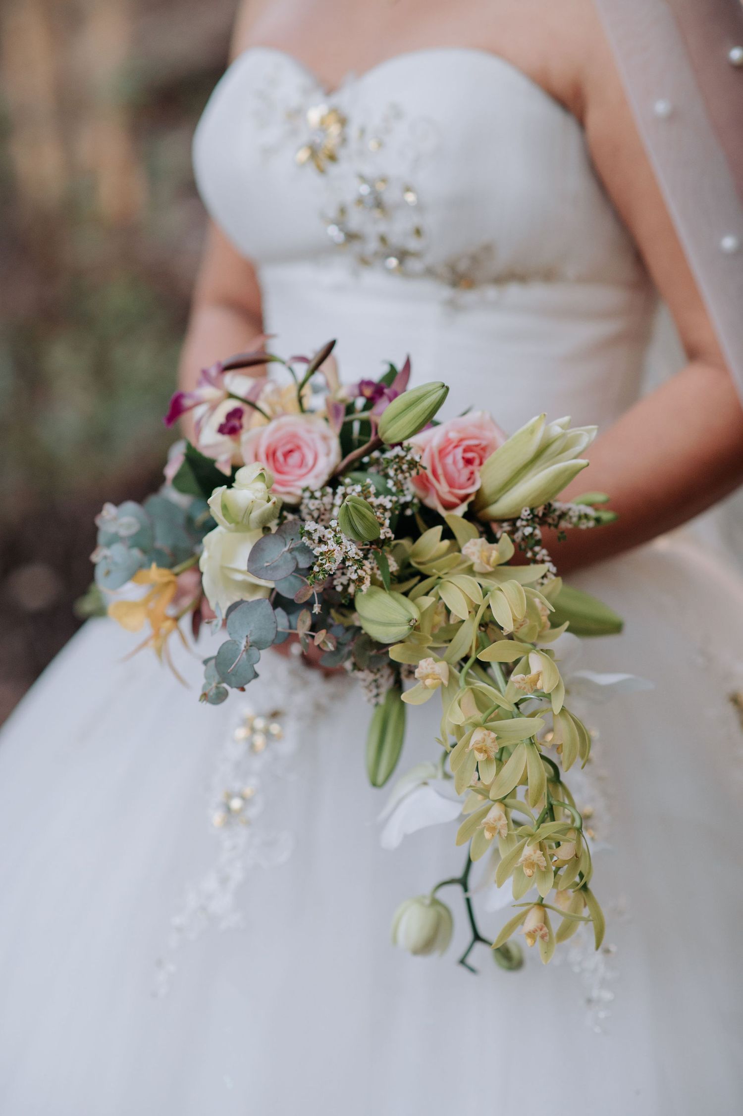 Elegant bridal bouquet features pink roses, orchids and eucalyptus against a white wedding dress.