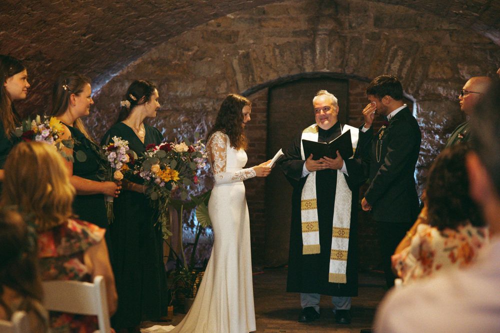 Intimate wedding ceremony in historic stone cellar with formal attire and floral decorations.