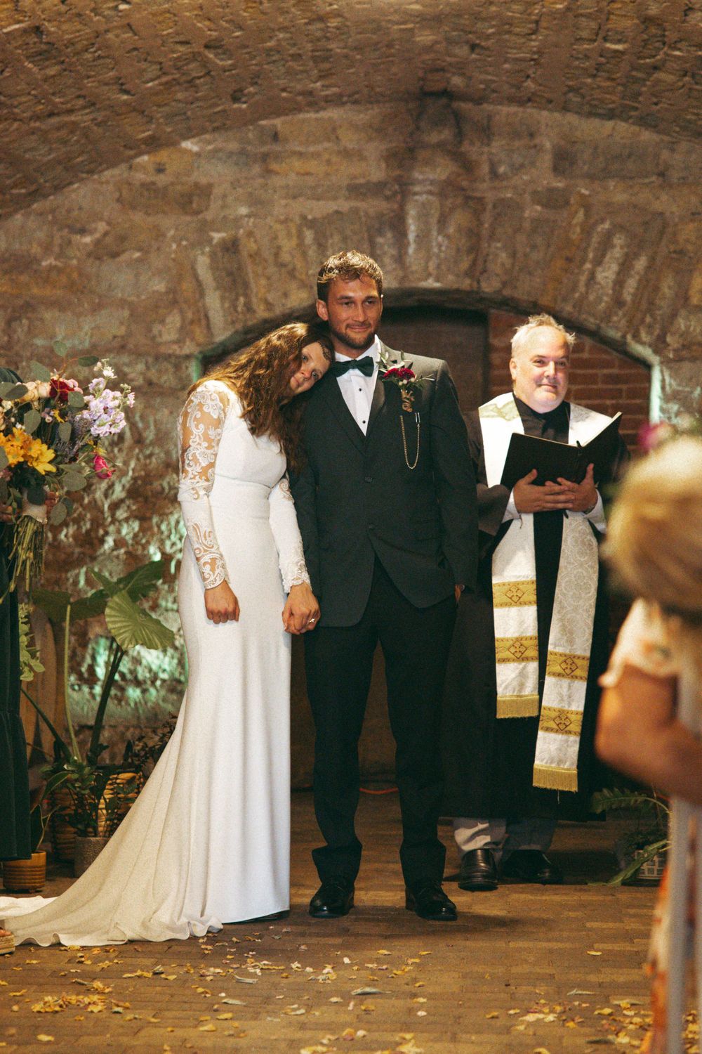 Wedding ceremony in rustic stone cellar with elegant white dress and classic black tuxedo.