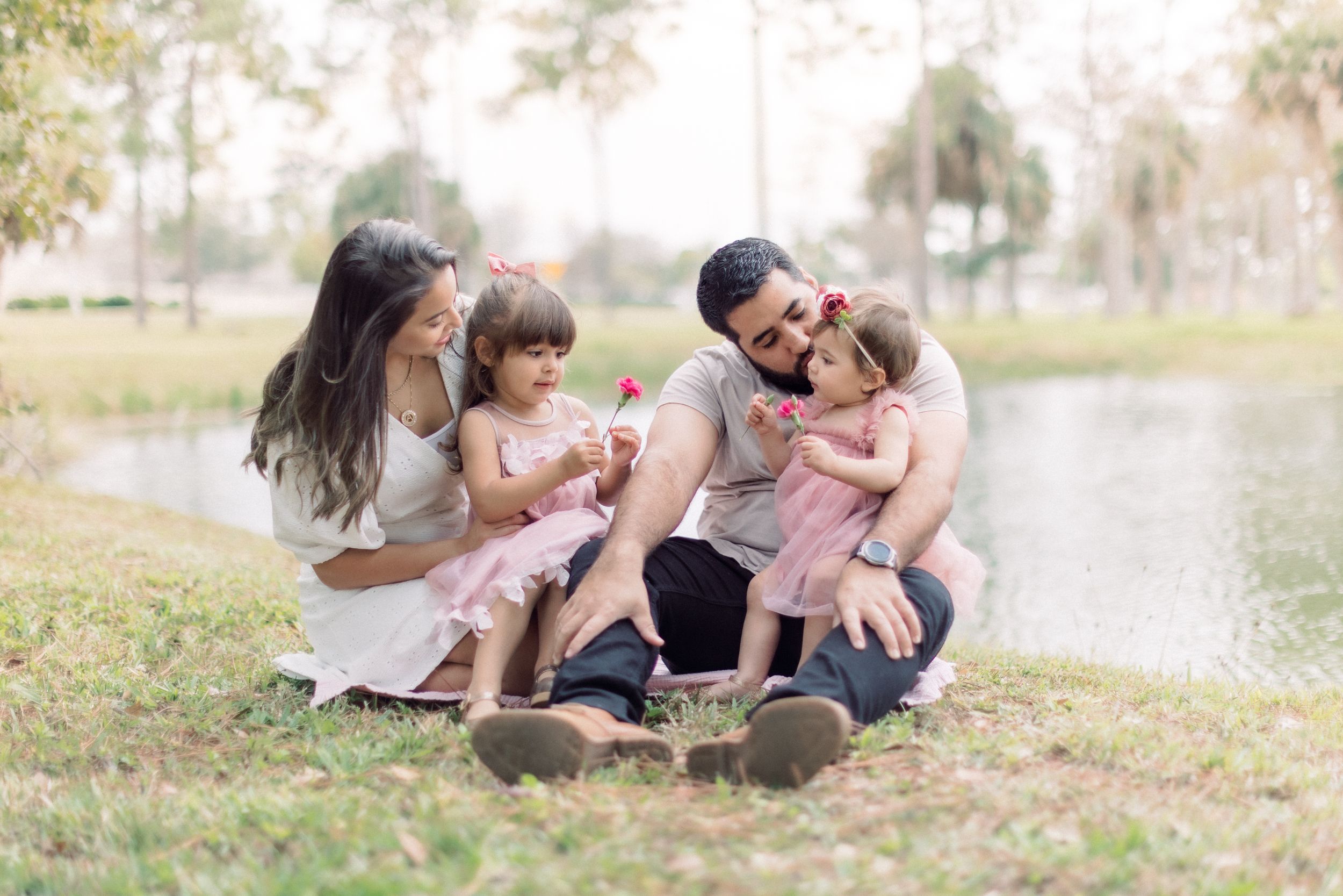 A happy family enjoying quality time together while sitting on grass near a pond.