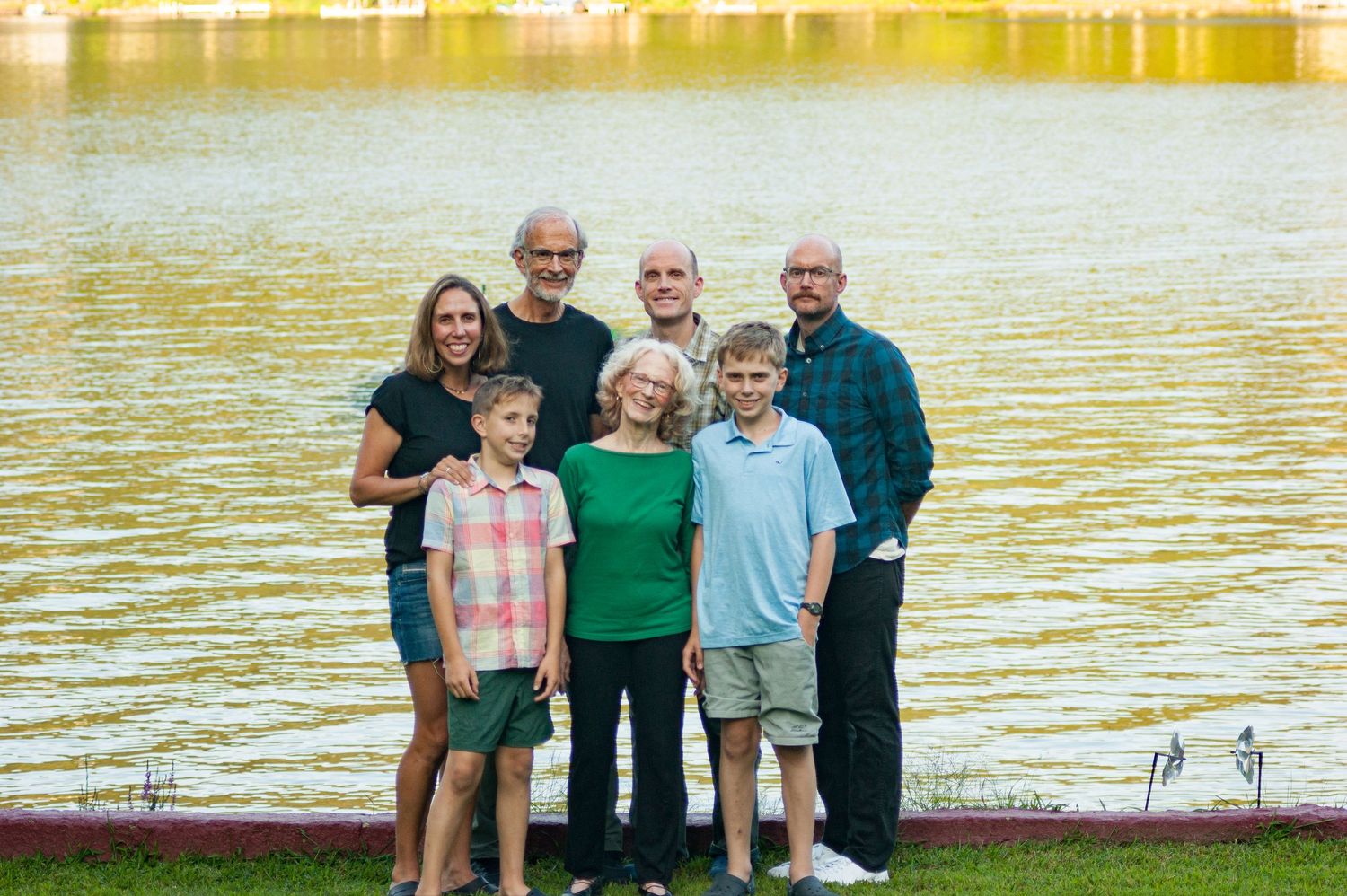 Extended family gathering at lakeside during golden hour with water and trees in background.