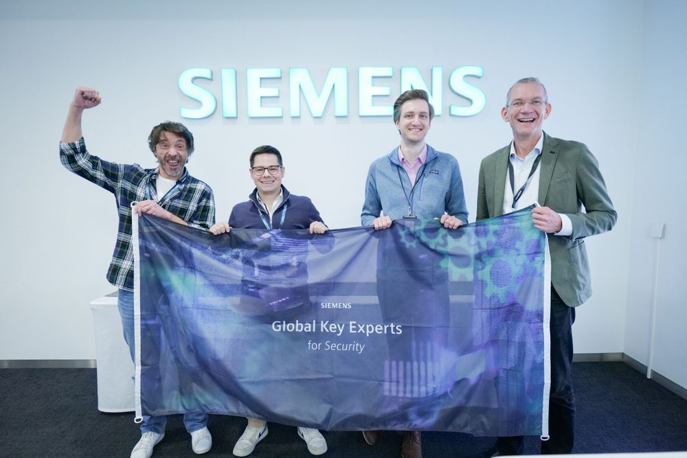 Four Siemens Global Key Experts for Security pose with branded flag in front of Siemens logo.