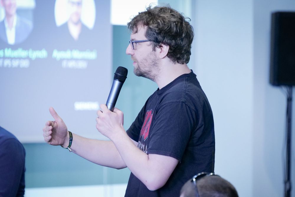 Male attendee in black t-shirt asks question with microphone at Siemens corporate event.