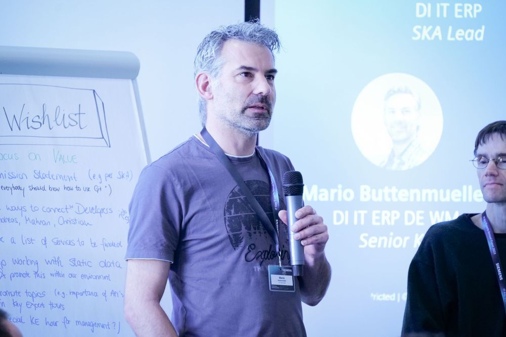 Male speaker presenting at a business meeting with DI IT ERP SKA Lead title displayed.